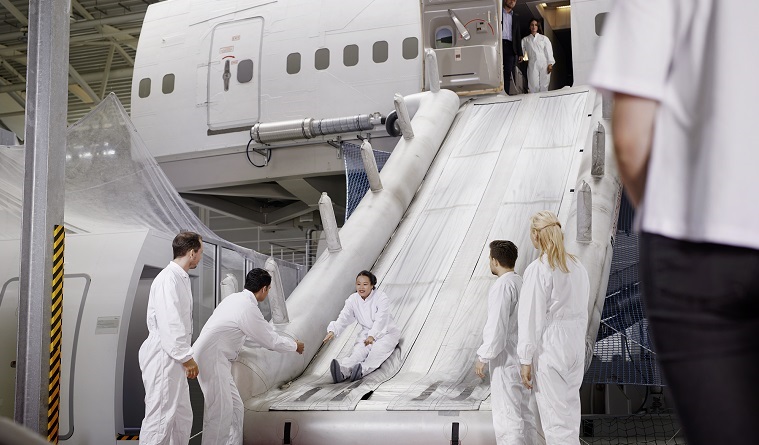 Several people are training by sliding down the emergency slide of an aircraft mock-up