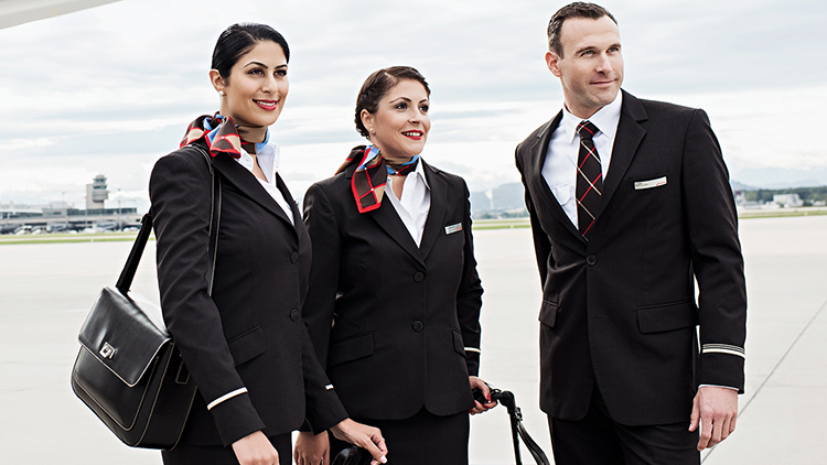 Two female and one male SWISS flight attendants stand with their luggage on a runway.