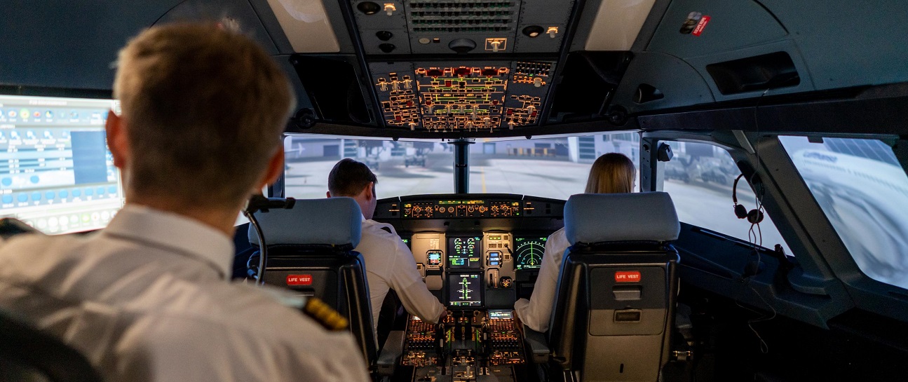 View into the cockpit of a flight simulator with two pilots and an instructor.
