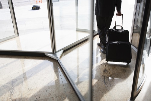 A person walks through a revolving door with a rolling suitcase