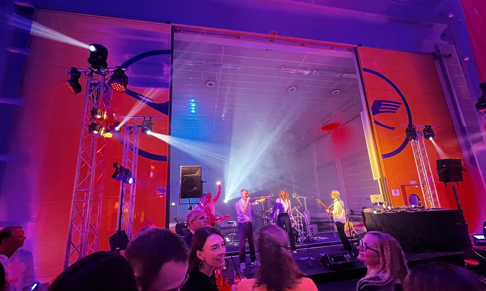Eine Band spielt, im Vordergrund stehen Personen.