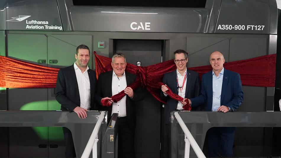 Vier Personen stehen vor einem Flugsimulator, der mit einer Schleife eingewickelt ist.