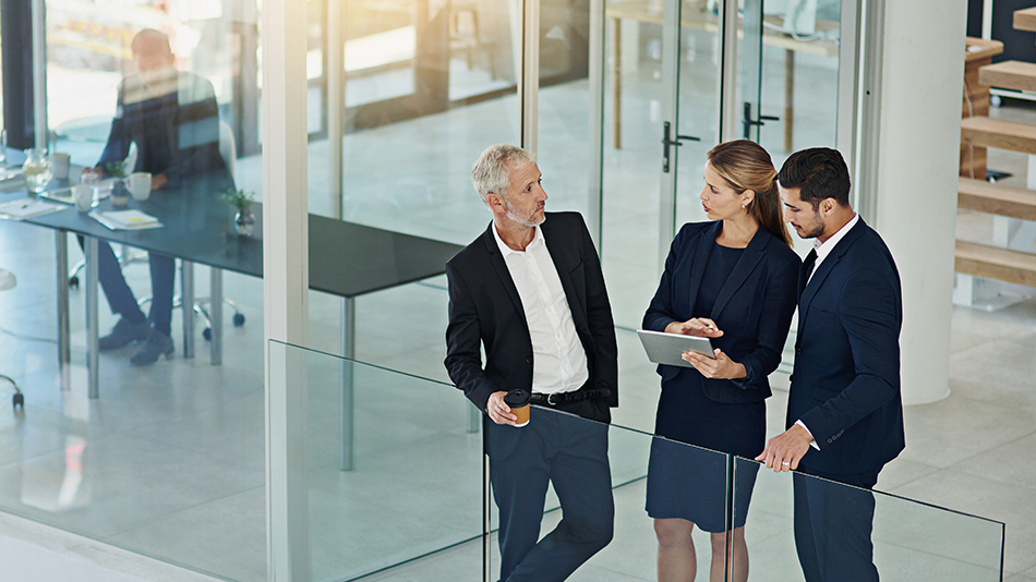 Drei Personen in Business-Kleidung stehen an einer Glaswand.
